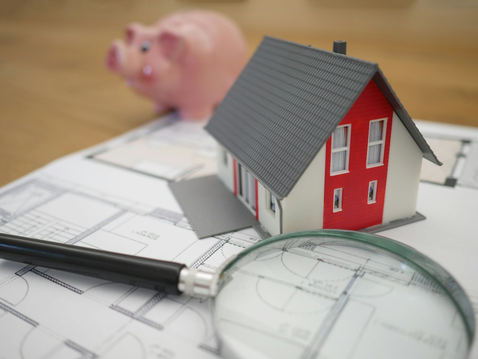House model with a magnifying glass over property blueprints